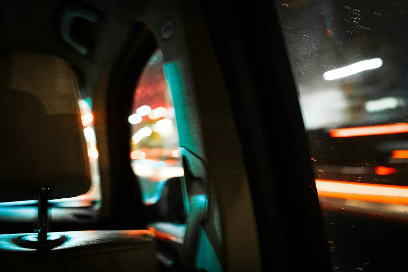 Teal and amber city lights passing a car window, viewed from the back seat